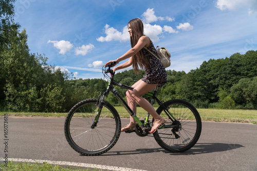 Girl riding a bicycle. Side view. Forest and clouds in the background