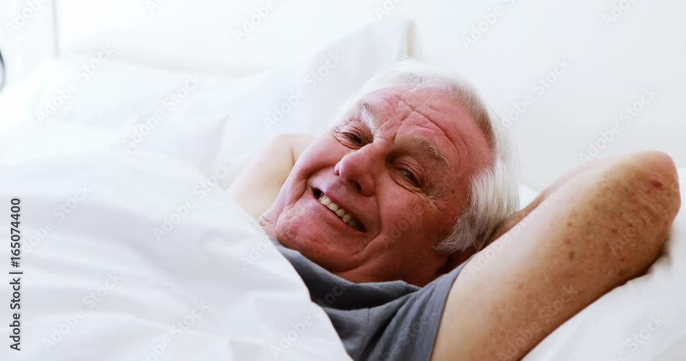 Smiling senior man lying on bed in bedroom Smiling senior man lying on bed in bedroom