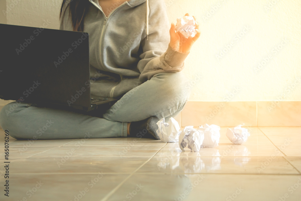 Woman sitting floor using laptop and crumpled paper.