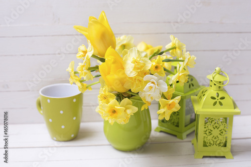 Yellow spring daffodils or narcissus flowers in green pitcher and decorative green lanterns