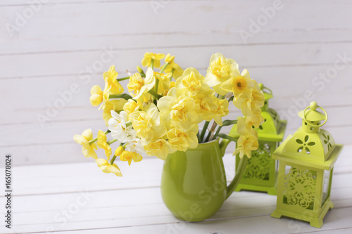 Fototapeta Naklejka Na Ścianę i Meble -  Yellow spring daffodils or narcissus flowers in green pitcher and decorative green lanterns