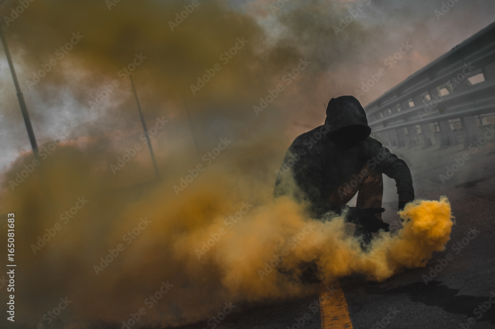A brutal guy in a sweatshirt with colored smoke posing on the bridge magnificent advertising of colored smoke A brutal guy in a sweatshirt with colored smoke posing on the bridge magnificent advertising of colored smoke