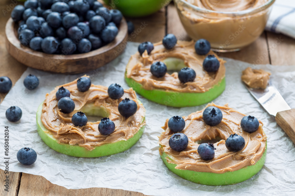 Green apple rounds with peanut butter and and blueberries on wooden table, horizontal Green apple rounds with peanut butter and and blueberries on wooden table, horizontal