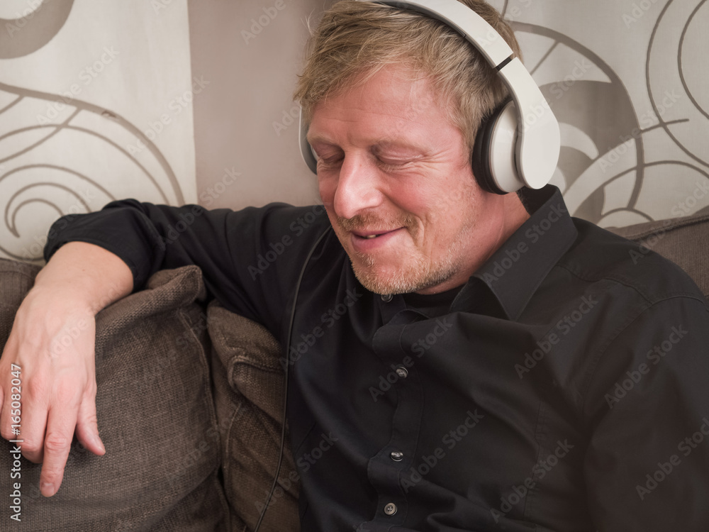 Obraz premium Mature man with white headphones on a couch.