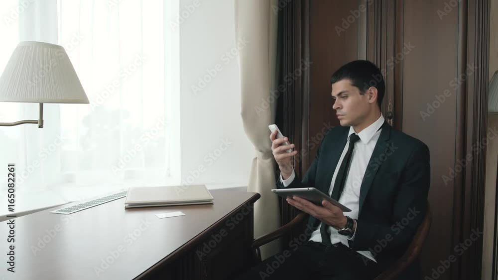 Serious businessman using some application on digital tablet at home, handsome business man in modern hotel work near window Serious businessman using some application on digital tablet at home, handsome business man in modern hotel work near window