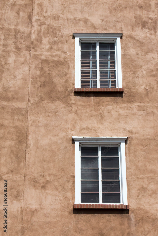 Two white windows in brown adobe wall