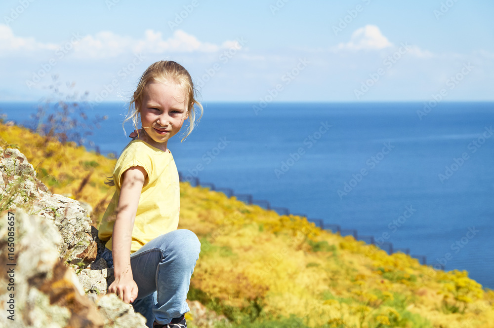 Nice blonde girl posing on the shore of a lake among the yellow flowers 