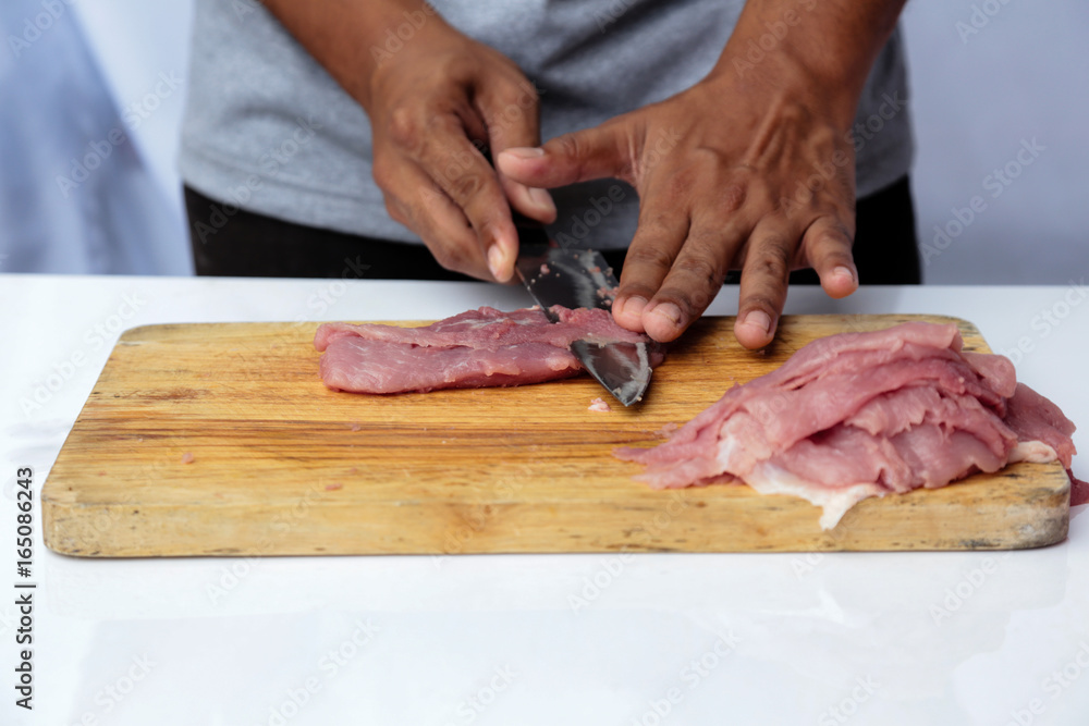Chef cutting pork on a wooden chopping board with a very sharp knife.