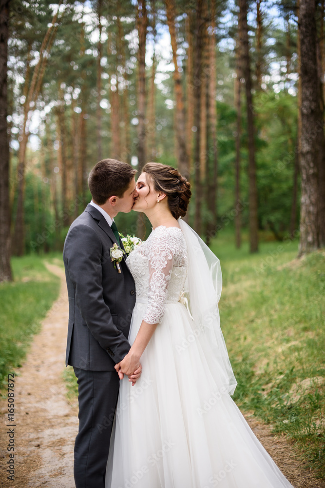 Just married loving couple in wedding dress and suit  in a forest. happy bride and groom walking and kissing 