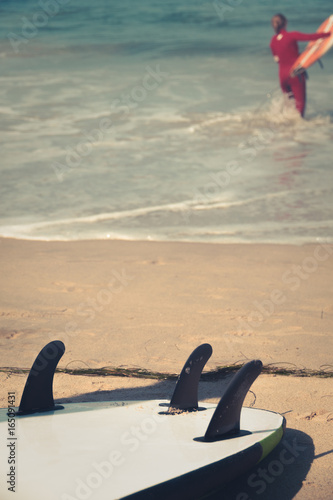 Surfboard on sandy beach with surder in background