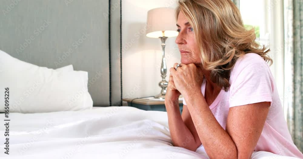 Thoughtful woman siting on bed in bedroom Thoughtful woman siting on bed in bedroom
