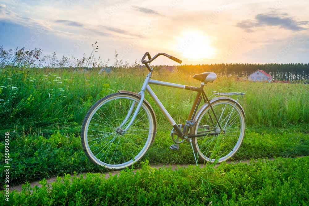 Old bicycle in the field against a background of tall grass and beautiful sunset