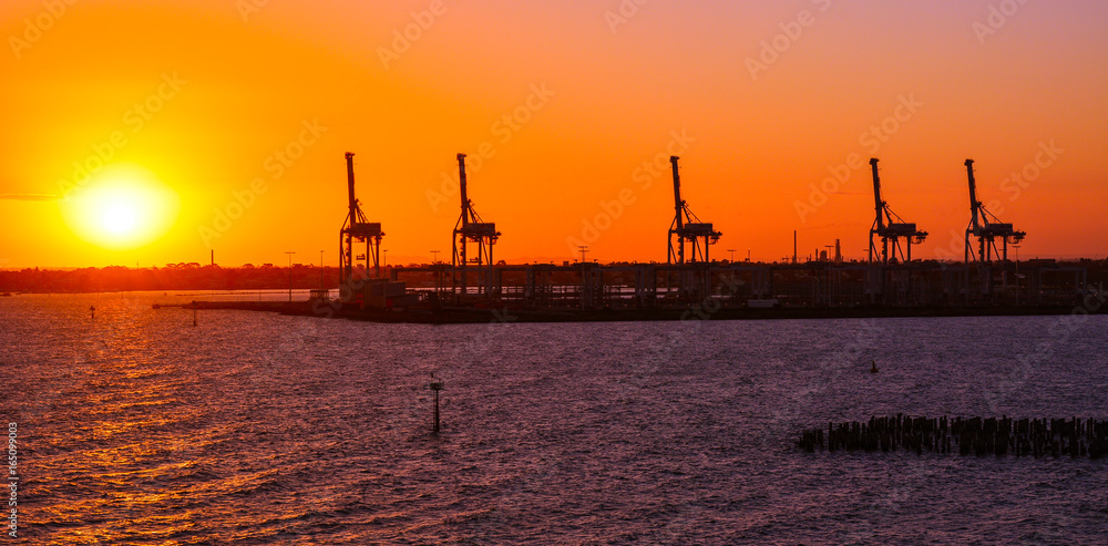 Container-handling gantry cranes silhouetted against setting sun - Melbourne, Australia