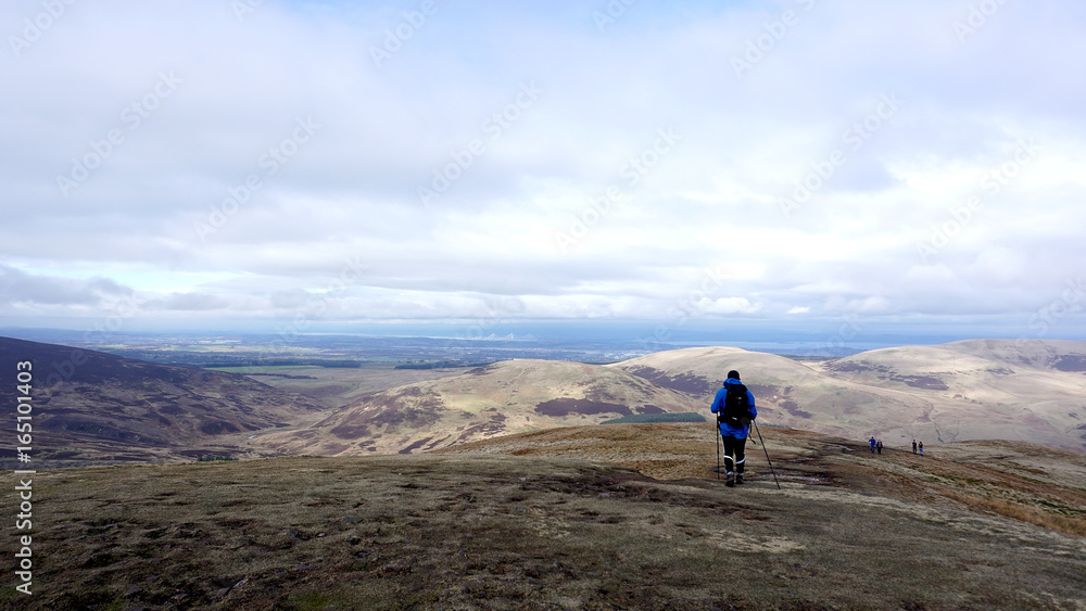 Hill walker on a country path looking down towards a lake in a country landscape. 