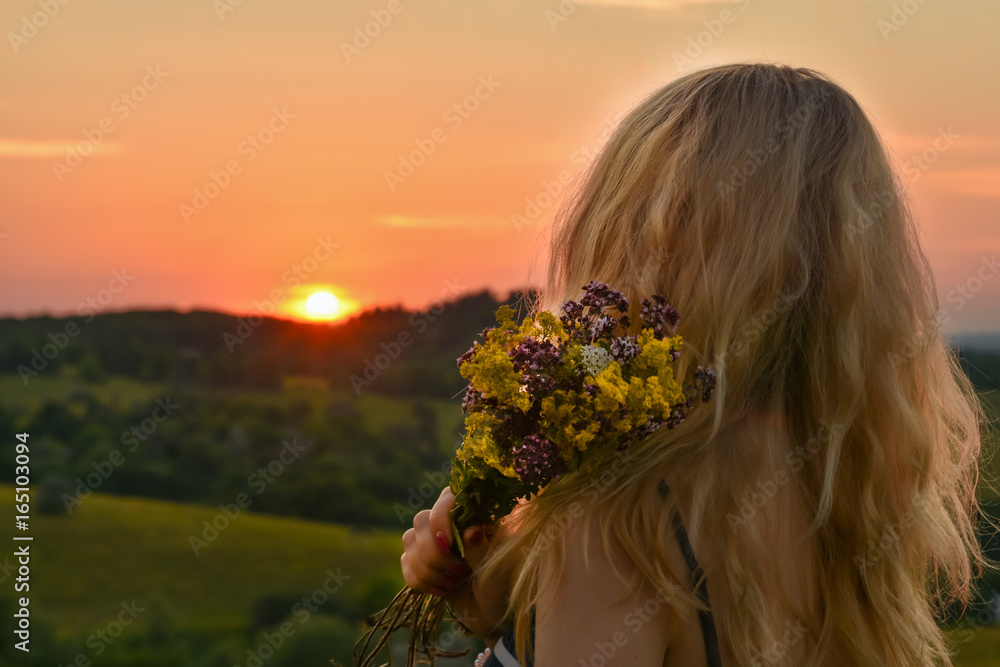 Naklejka premium Background landscape girl holding a bouquet with wildflowers of herbs in her hand and watching the sunset sunrise on the horizon