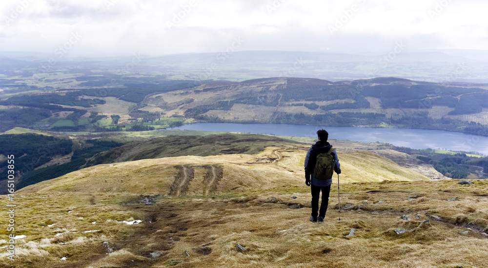 Hill walker on a country path looking down towards a lake in a country landscape at Pentland Hills, Edinburgh, Scotland 