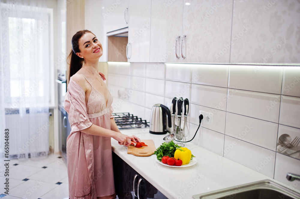 Portrait of an attractive young woman in robe making salad out of fresh vegetables in the kitchen. Portrait of an attractive young woman in robe making salad out of fresh vegetables in the kitchen.