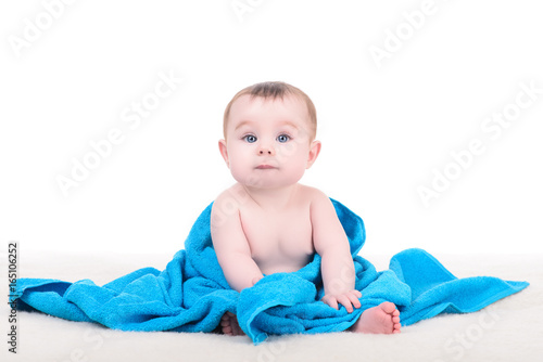 Adorable baby girl or boy with big blue eyes sitting on soft blanket, wrapped in blue towel, isolated on white