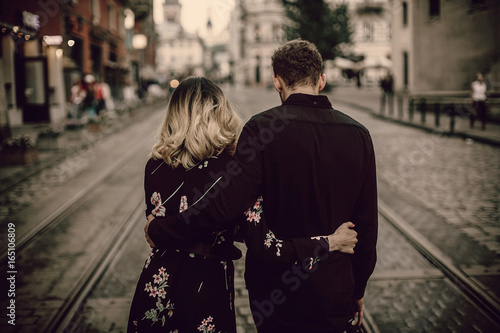 stylish gypsy couple in love walking and hugging in evening city street. woman and man gently embracing, romantic french atmospheric moment. love mood. back view