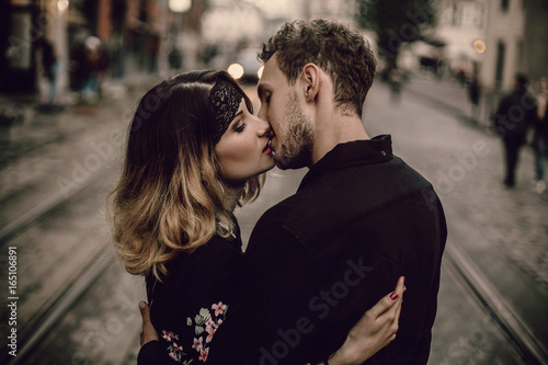 stylish gypsy couple in love kissing hugging in evening city street. woman and man gently embracing, romantic french atmospheric moment. love mood. gypsy wedding.