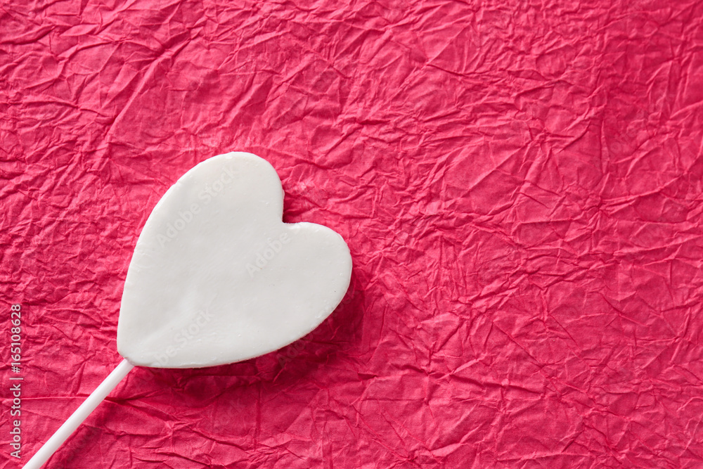 Fototapeta premium Tasty candy in shape of heart on color crumpled paper