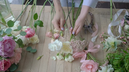 Hands of female florist arranging flower bouquet over a wooden table. Top view