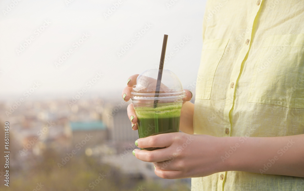 Woman holding cup of green smoothie on street Woman holding cup of green smoothie on street