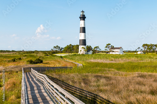 Wooden ramp over marshland, with a boardwalk trail to the Bodie Island lighthouse and surrounding buildings, on the Outer Banks of North Carolina near Nags Head.   photo