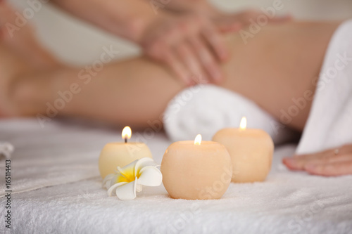 Burning candles with beautiful flower and blurred woman having legs massage in spa salon on background