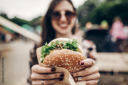 Close up of woman's hands holding cheeseburger outdoors