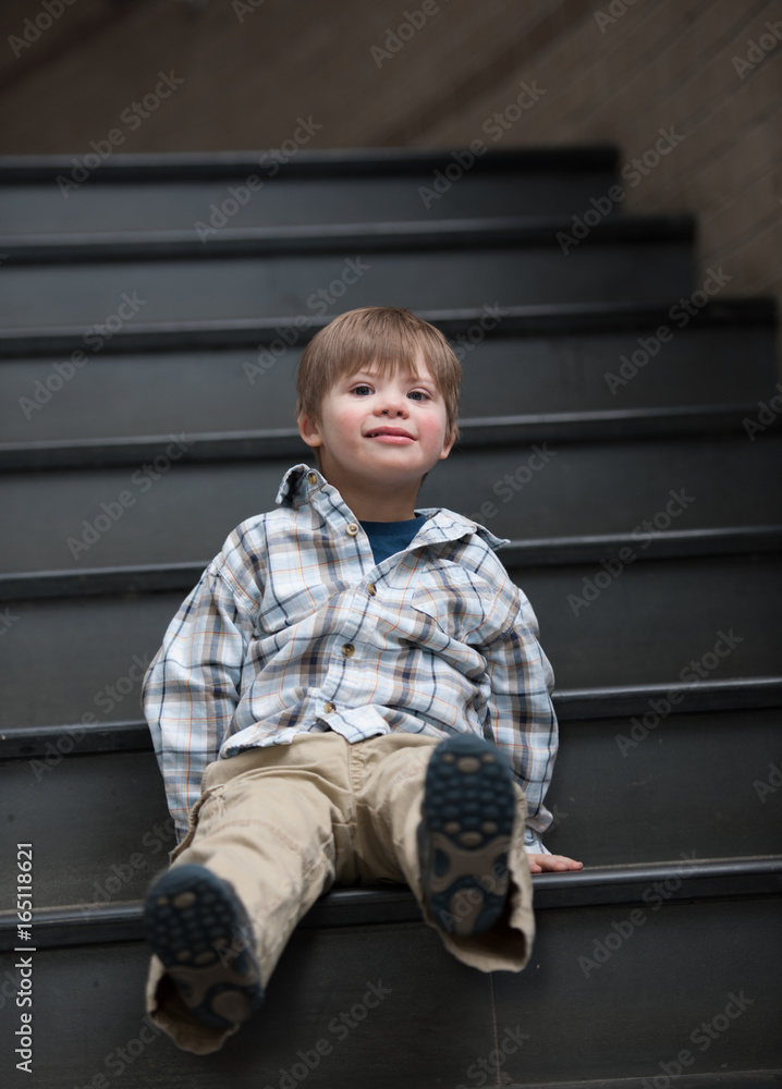 Kindergarten Boy with Down Syndrome Sits on School Stairwell Kindergarten Boy with Down Syndrome Sits on School Stairwell