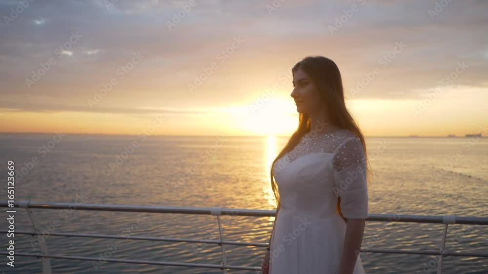Beauty girl on sky background in a white dress in the sea. beautiful bride, model eyes, sun rise on the beach wedding. Wedding dress, apparel developing sea breeze. Slow motion Beauty girl on sky background in a white dress in the sea. beautiful bride, model eyes, sun rise on the beach wedding. Wedding dress, apparel developing sea breeze. Slow motion