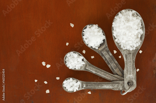 Old tarnished measuring spoons filled with sea salt on wood table photo