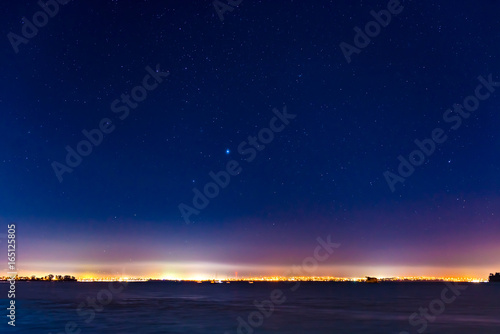 mist and a starry sky above the lights of a city skyline on the waterfront in Auckland, New Zealand