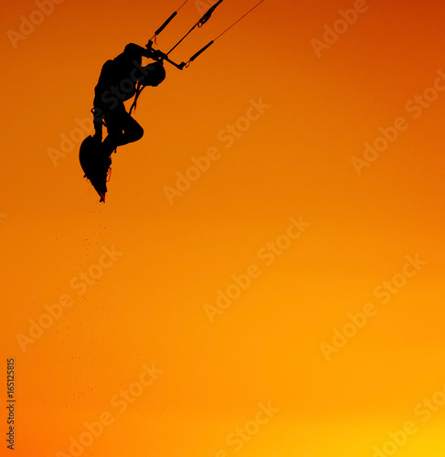 Kiteboarder sportsman with kite under sunset sun, freestyle kiteboarding rider on the evening kitesession, sunset in the sea, watersports, active lifestyle, extreme contrast colors black and orange