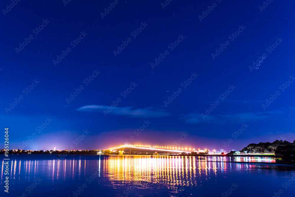cars in motion on a lighted bridge over the sea with a starry sky, boats in Auckland, New Zealand