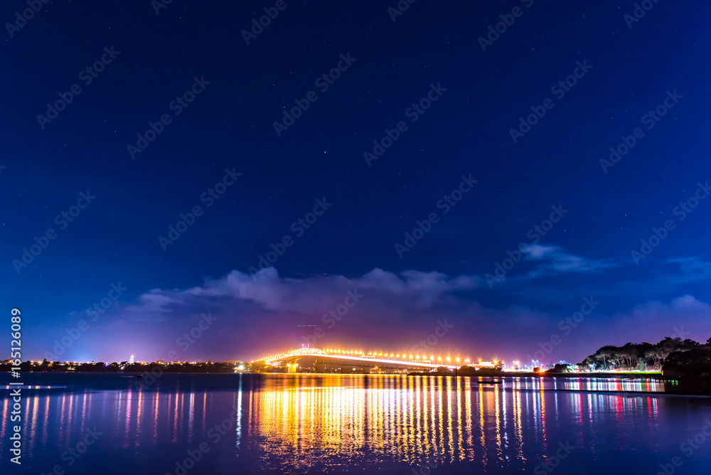 cars in motion on a lighted bridge over the sea with a starry sky, boats in Auckland, New Zealand