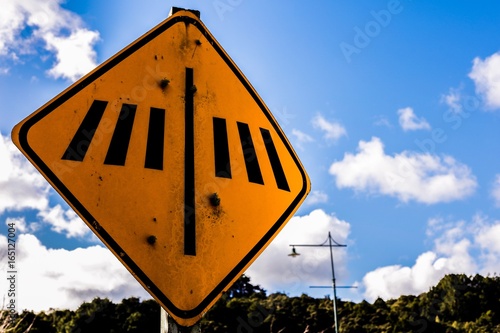 Sign: Pedestrian Crossing, yellow. Blue cloudy sky and trees in background