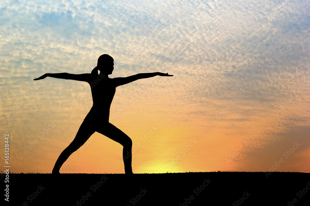 Silhouette of woman practicing warrior yoga at sunset