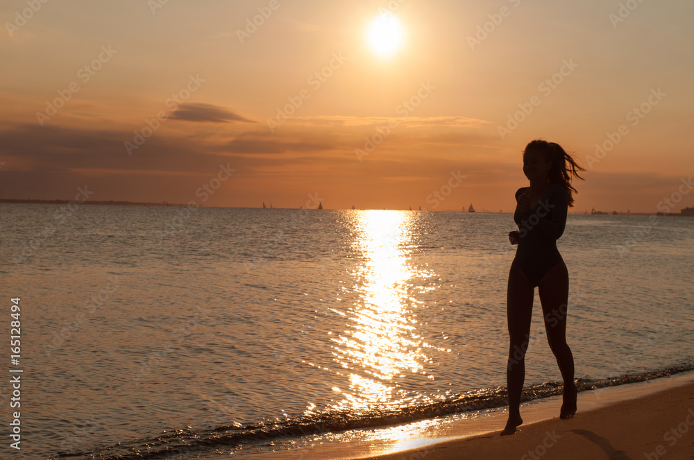 Silhouette of a young woman running on the seaside at sunset