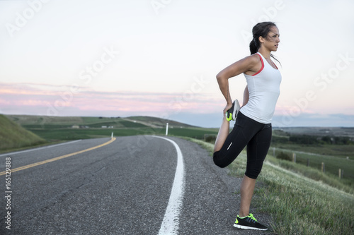 a young athletic woman stretching on the side of a paved road