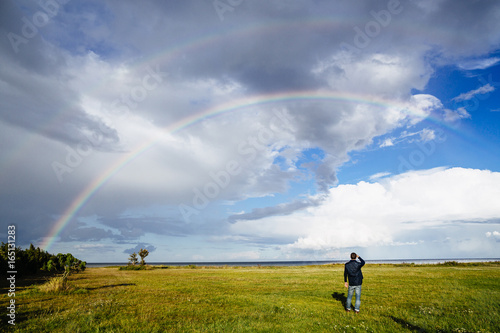 Man standing in a meadow watching rainbow