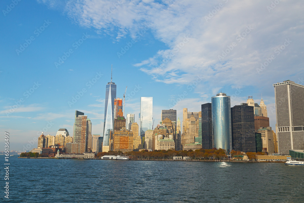 Panorama of Lower Manhattan from the water, New York, USA. Skyscrapers of Manhattan are illuminated by afternoon sun.