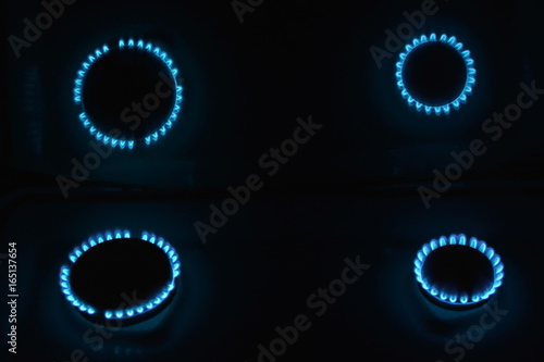 burning gas stove hob blue flames close up in the dark with inverted reflection in mirror on a black background