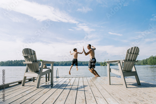 Boy and dad high five as they leap off a dock together