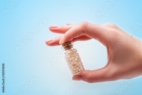 Woman hands holding a bottle with homeopathic pills on white background