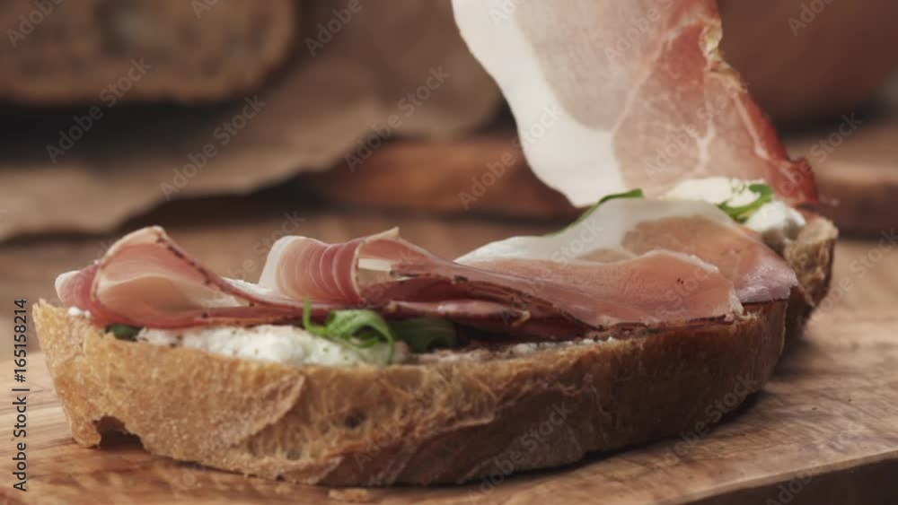 Slow motion of italian speck put on rustic bread with arugula and ricotta cheese