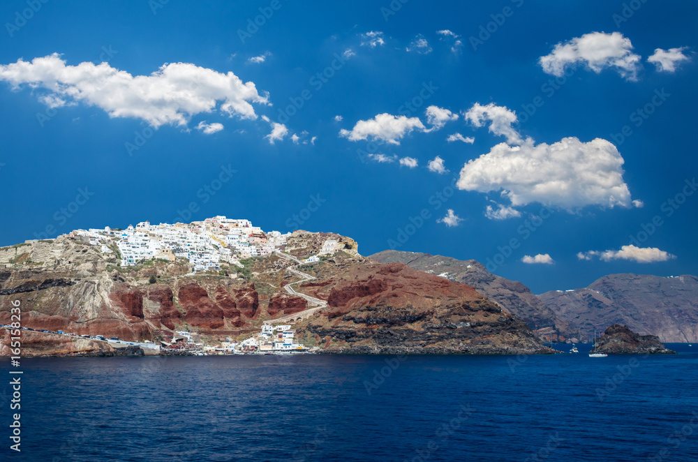 Oia Village, Santorini Cyclade islands, Greece. Beautiful view of the town with white buildings, blue church's roofs and many colored flowers.