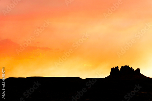 single mesa or rock formation in silhouette against a beautiful red and orange evening sky