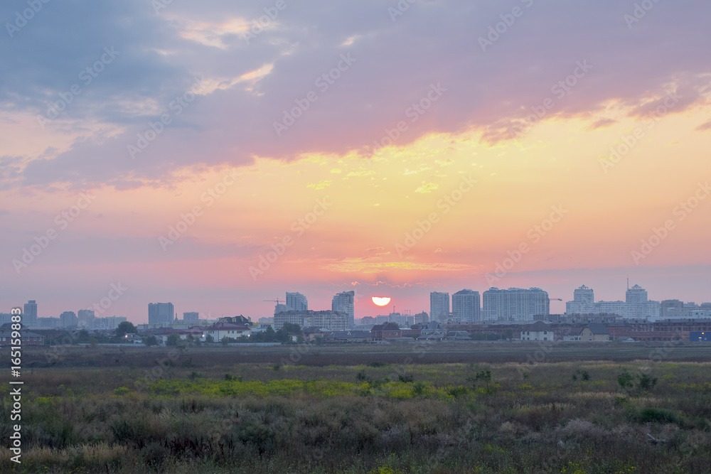 Delicate colors of sunrise over the city, sun down. Panoramic view of the field and sky in the morning, the sun half closed by a cloud rising above the city